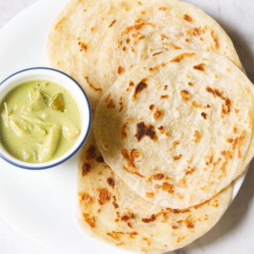 kerala parotta placed on white plate with a bowl of green curry at left side.