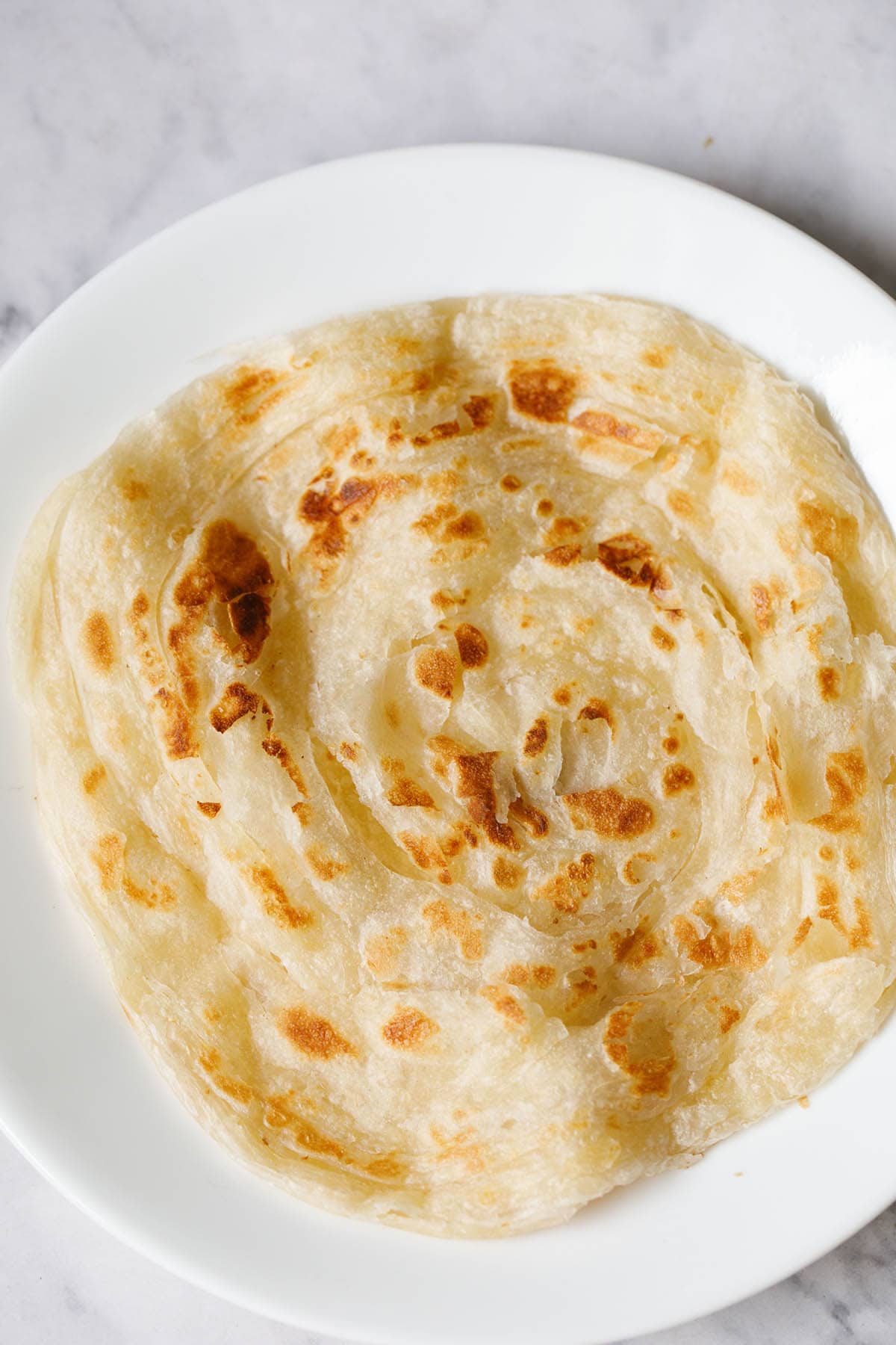 malabar paratha served on a white plate.