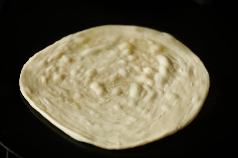 roasting prepared malabar paratha on a hot tawa. 