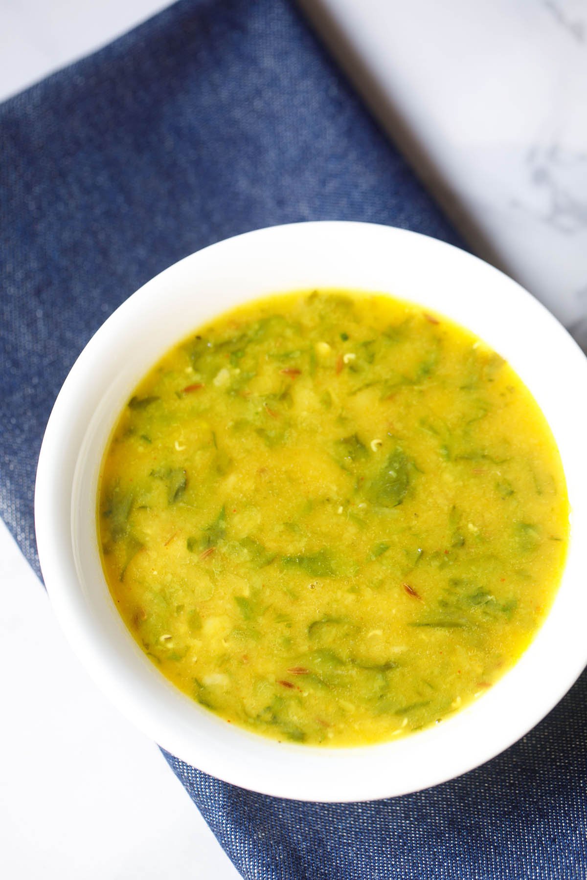 dal palak served in a white bowl on a dark blue napkin.