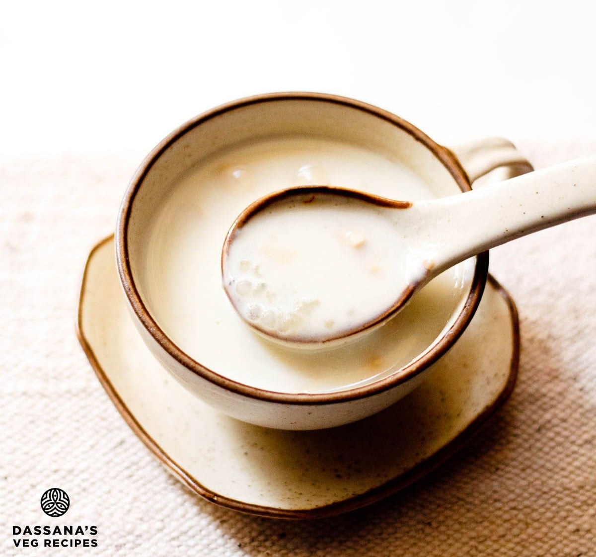 Creamy sabudana kheer in a spoon over a bowl filled with the sago kheer.