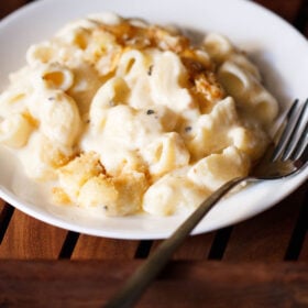 mac and cheese in a deep white plate with fork on the right side.