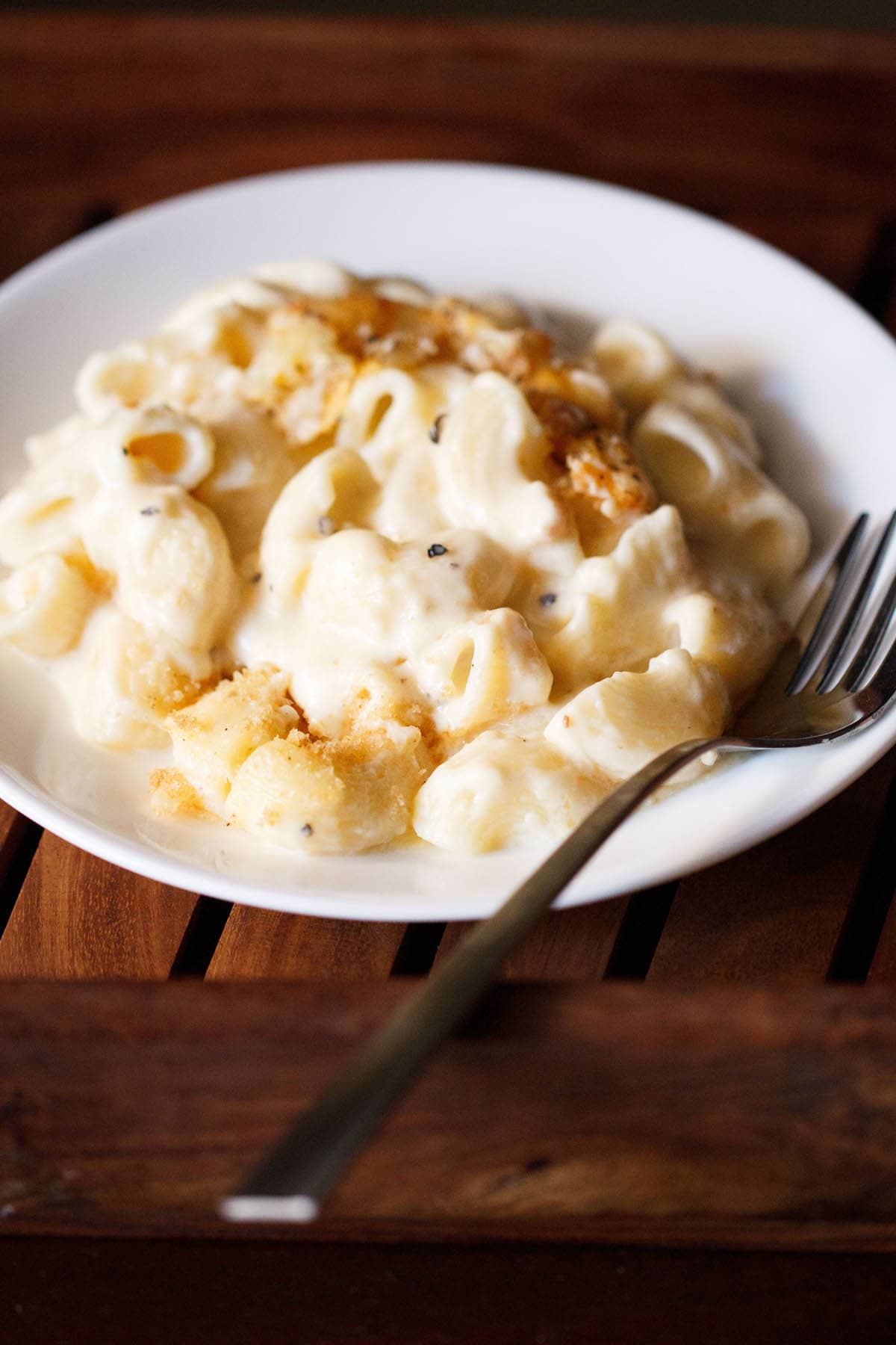 mac and cheese in a deep white plate with fork on the right side.