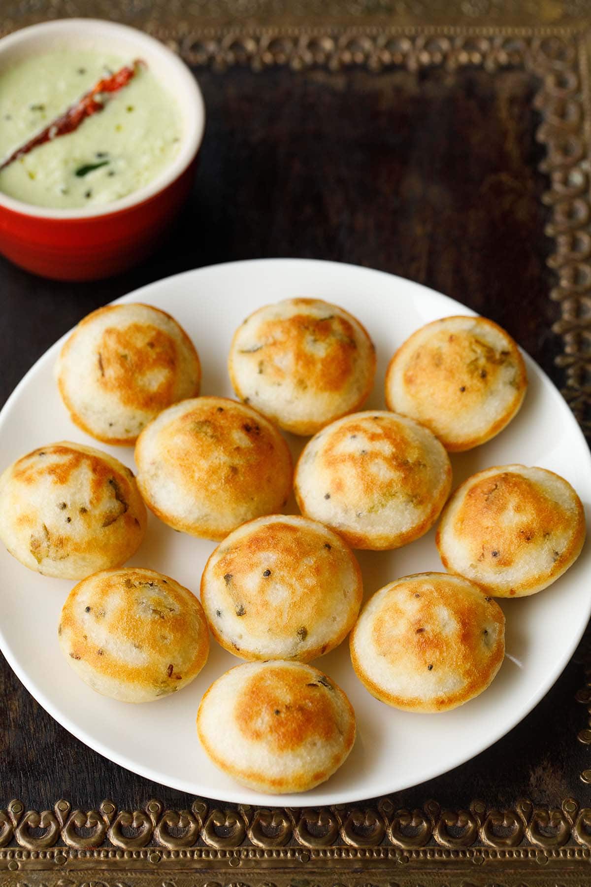 appe or paddu on a plate with coconut chutney in red bowl on top.