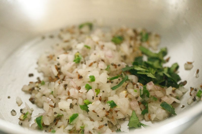 finely chopped onions, finely chopped green chilies, finely chopped curry leaves and asafoetida added to hot oil for making tempering for appe. 