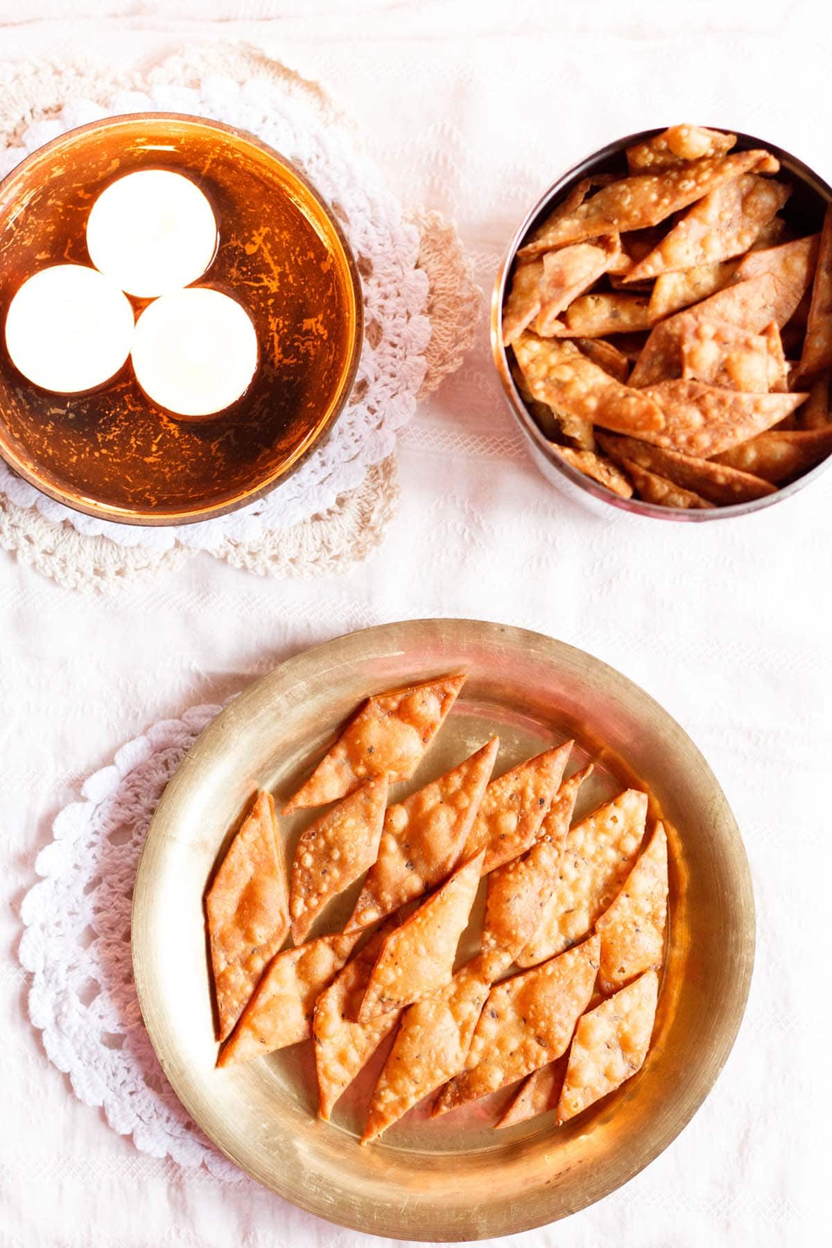 top shot of namak pare on a brass plate with lighted lamps in a bowl placed on water.