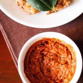 tomato chutney served in a small white bowl with a platter of pakoda kept on the top side.