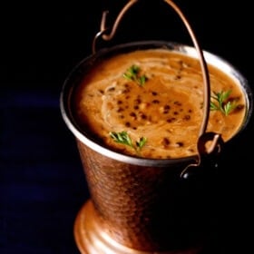 dal makhani garnished with coriander leaves and served in a fancy bucket with text layovers.