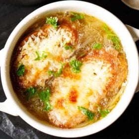 closeup image of french onion soup in a cream colored soup bowl, garnished with some parsley.