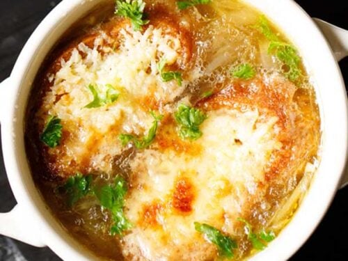 closeup image of french onion soup in a cream colored soup bowl, garnished with some parsley.