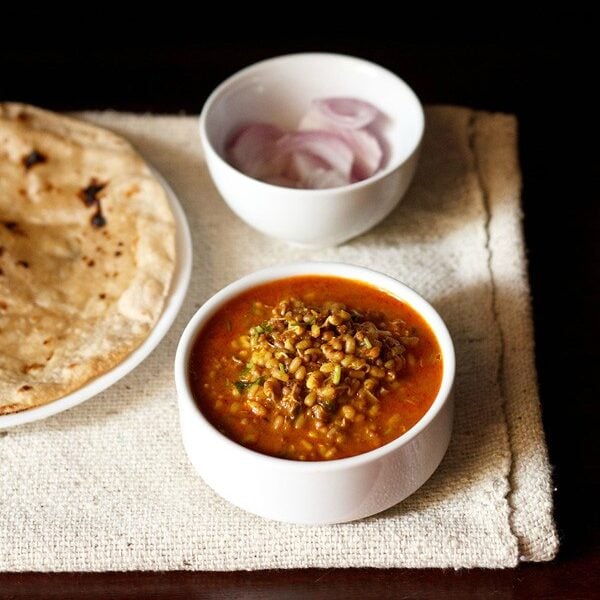 matki recipe served in a white bowl with a bowl of sliced onions and chapatis on a plate placed on the side and text layovers. 