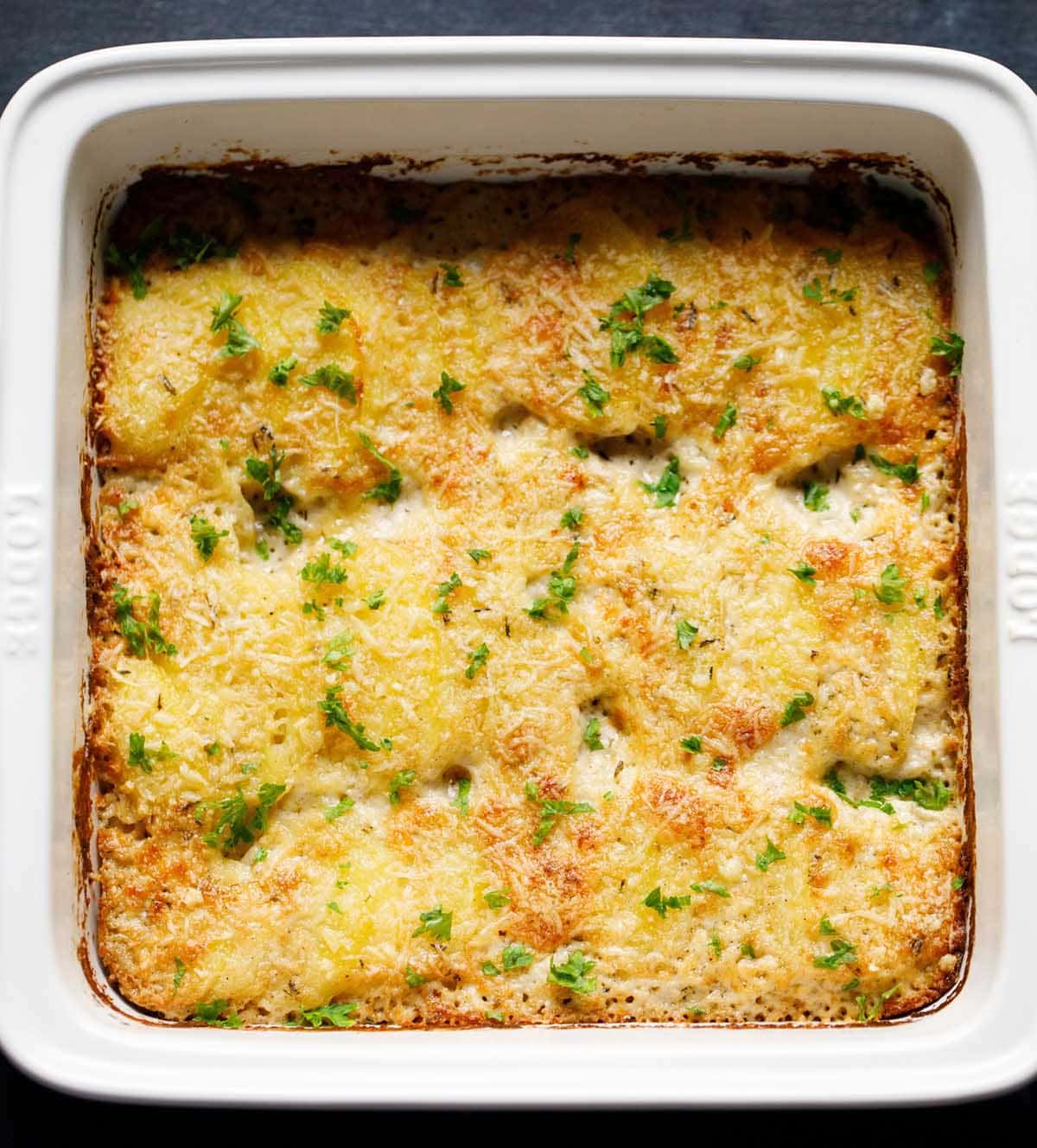 baked potato gratin garnished with parsley in a white baking pan.