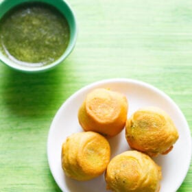 aloo bonda on a white plate with a small bowl of green chutney kept on the top side with text layovers.