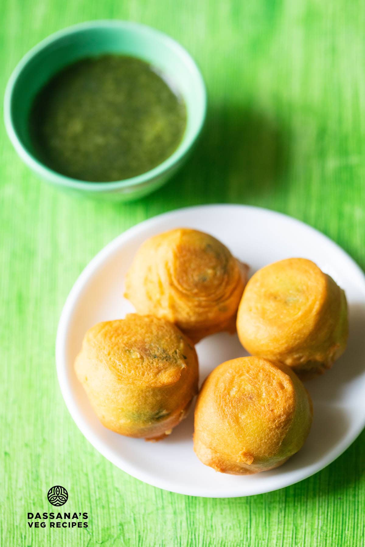 potato bonda served on a white plate with a small bowl of green chutney kept on the top side with text layovers.