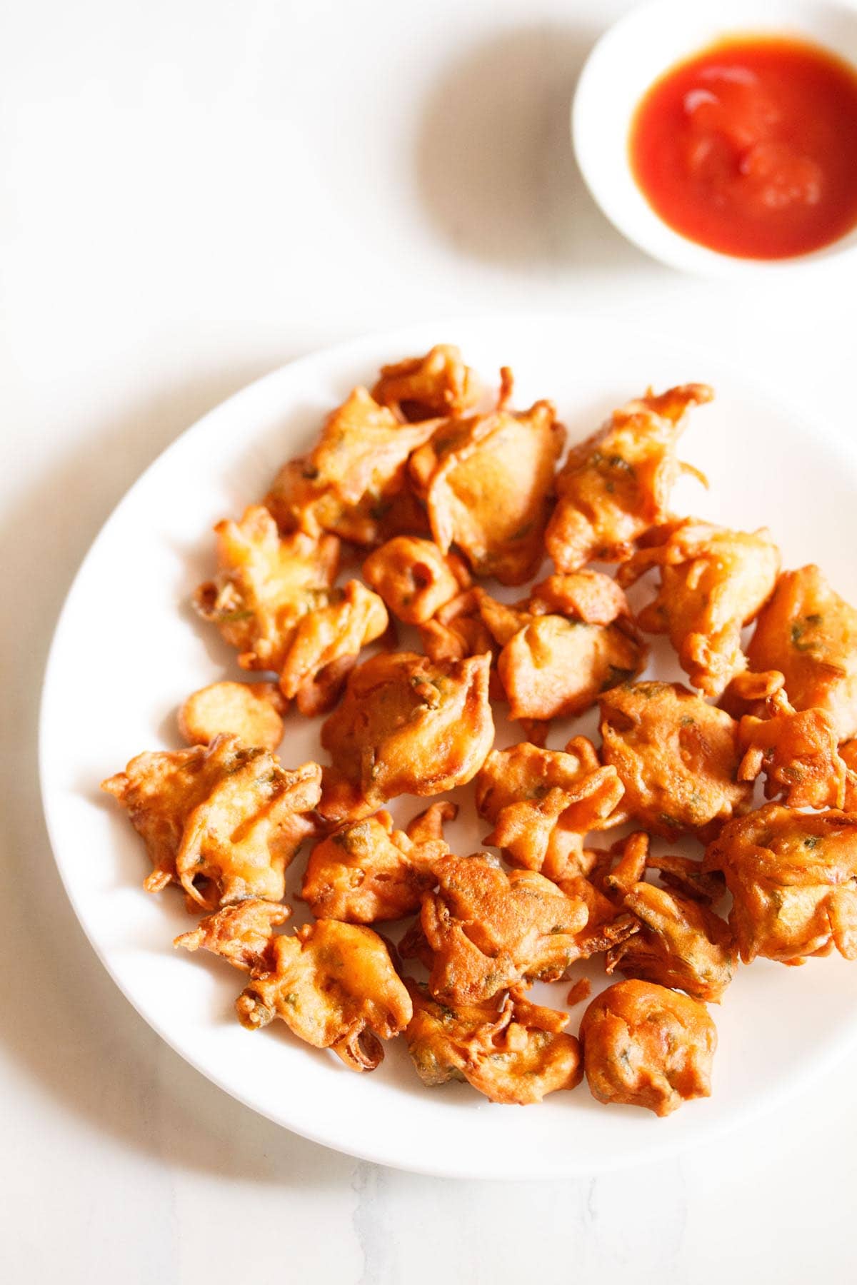 onion fritters served on a white plate with a small bowl of tomato ketchup on the side. 