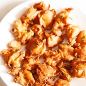 onion fritters served on a white plate with a small bowl of tomato ketchup on the side.