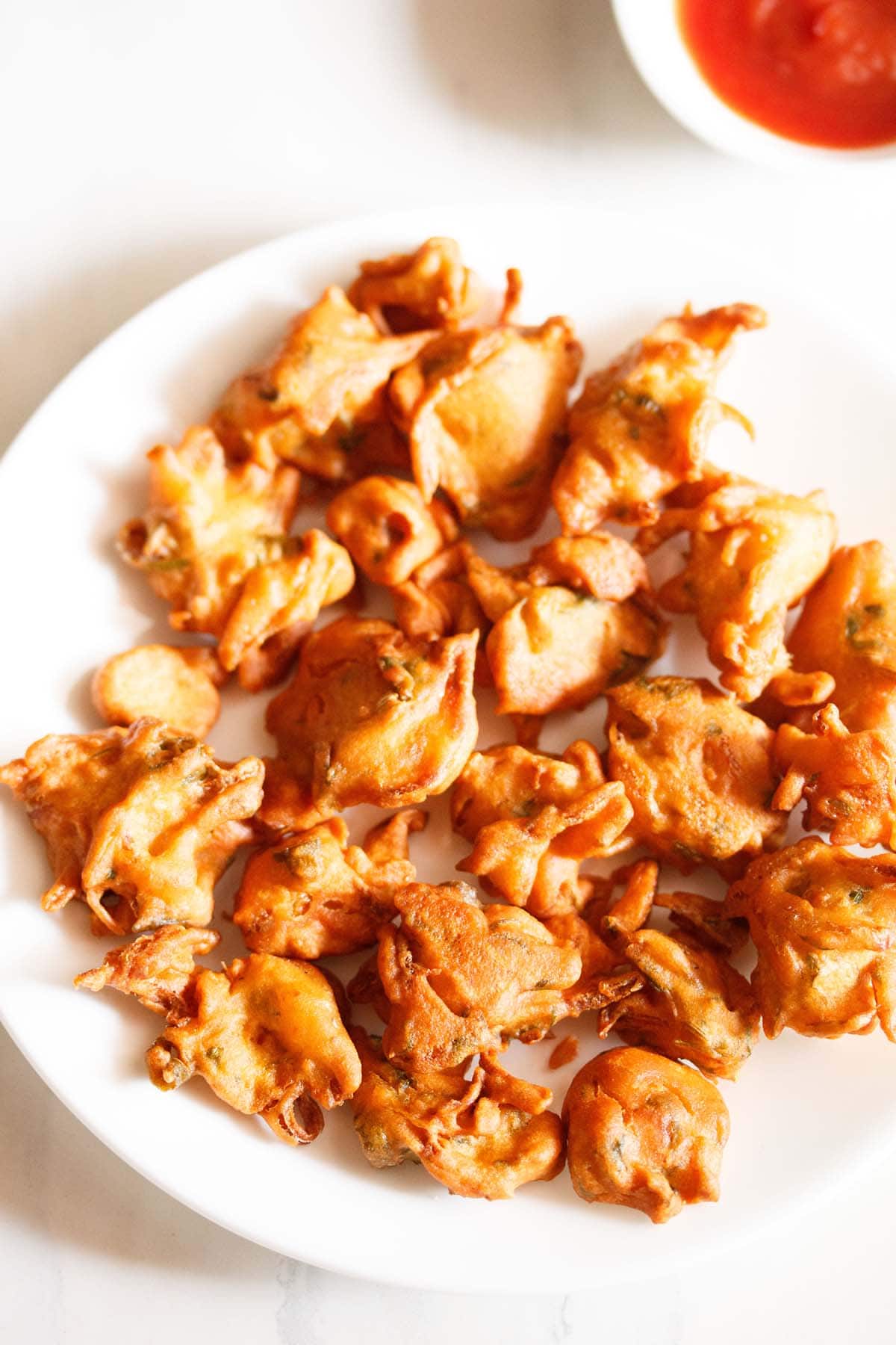 onion fritters served on a white plate with a small bowl of tomato ketchup on the side.