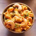 closeup image of vegetable curry topped with three cashews in a bowl.