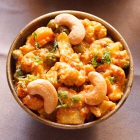 closeup image of vegetable curry topped with three cashews in a bowl.