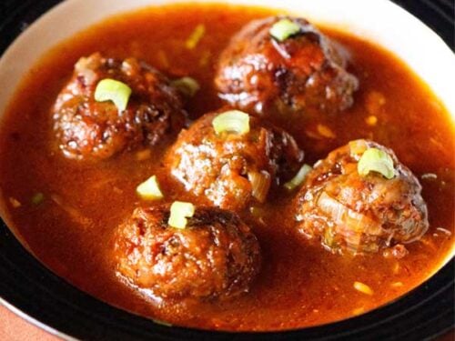 manchurian gravy garnished with chopped spring onion greens and served in a black rimmed bowl.