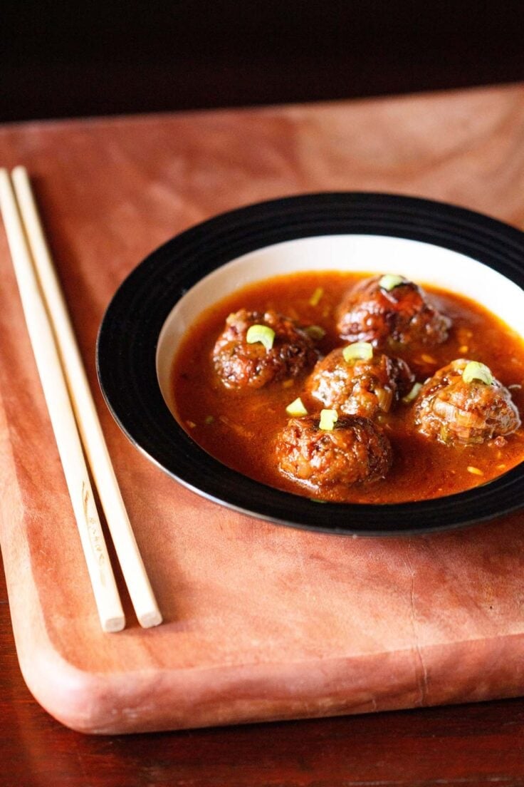 manchurian gravy garnished with chopped spring onion greens and served in a black rimmed bowl with chopsticks kept on the left side.