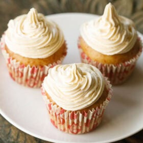 three buttercream frosted eggless cupcakes on a white plate in red and white cupcake liners.
