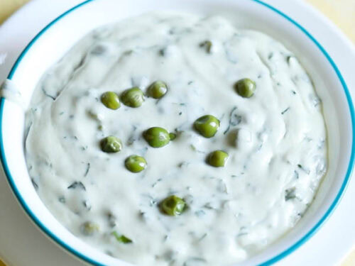 methi matar malai in a white bowl with a light blue rim, garnished with a few peas.