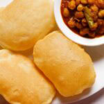 three bhatura with a side bowl of chana masala on a white plate.