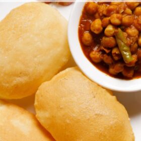 bhatura with a side bowl of chana masala and some masala onions by the side on a white plate.