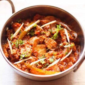 kadai mushroom garnished with coriander leaves, ginger juliennes and served in a steel kadai on a white napkin.