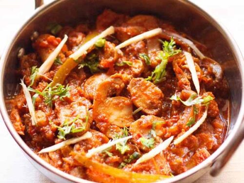 kadai mushroom garnished with coriander leaves, ginger juliennes and served in a steel kadai on a white napkin.