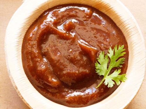 tamarind chutney in a bowl made of areca leaf garnished with a cilantro sprig.