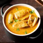 brinjal curry or baingan masala garnished with coriander leaves and served in a small black casserole.