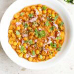 ghugni in white bowl topped with finely chopped onions, green chillies and coriander leaves.