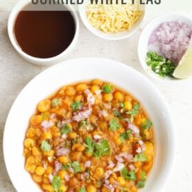 ghugni chaat in white bowl topped with finely chopped onions, green chilies, coriander leaves with three side bowls on top filled with tamarind water in first bowl, onions, chilies and lemon wedges in second bowl and sev in the third bowl with text layovers.