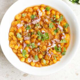 ghugni in white bowl topped with finely chopped onions, green chillies and coriander leaves.