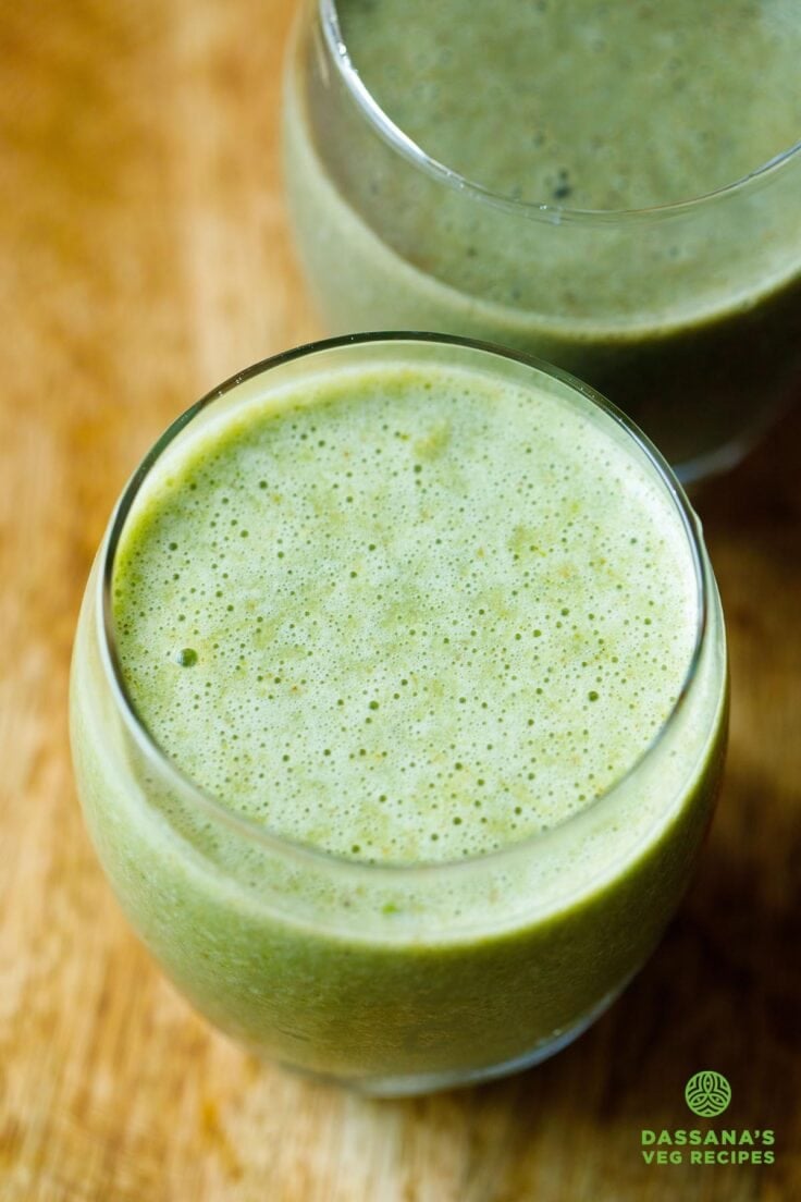 green smoothie in a round large glass with another green smoothie made with blueberries in a second glass placed on top.