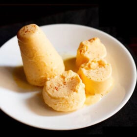 mango kulfi sliced and whole on a white plate on a black napkin.