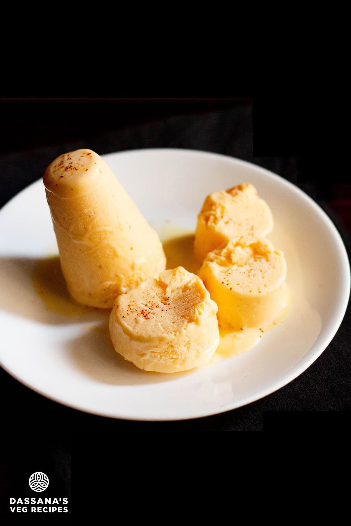 mango kulfi sliced and whole on a white plate on a black napkin.