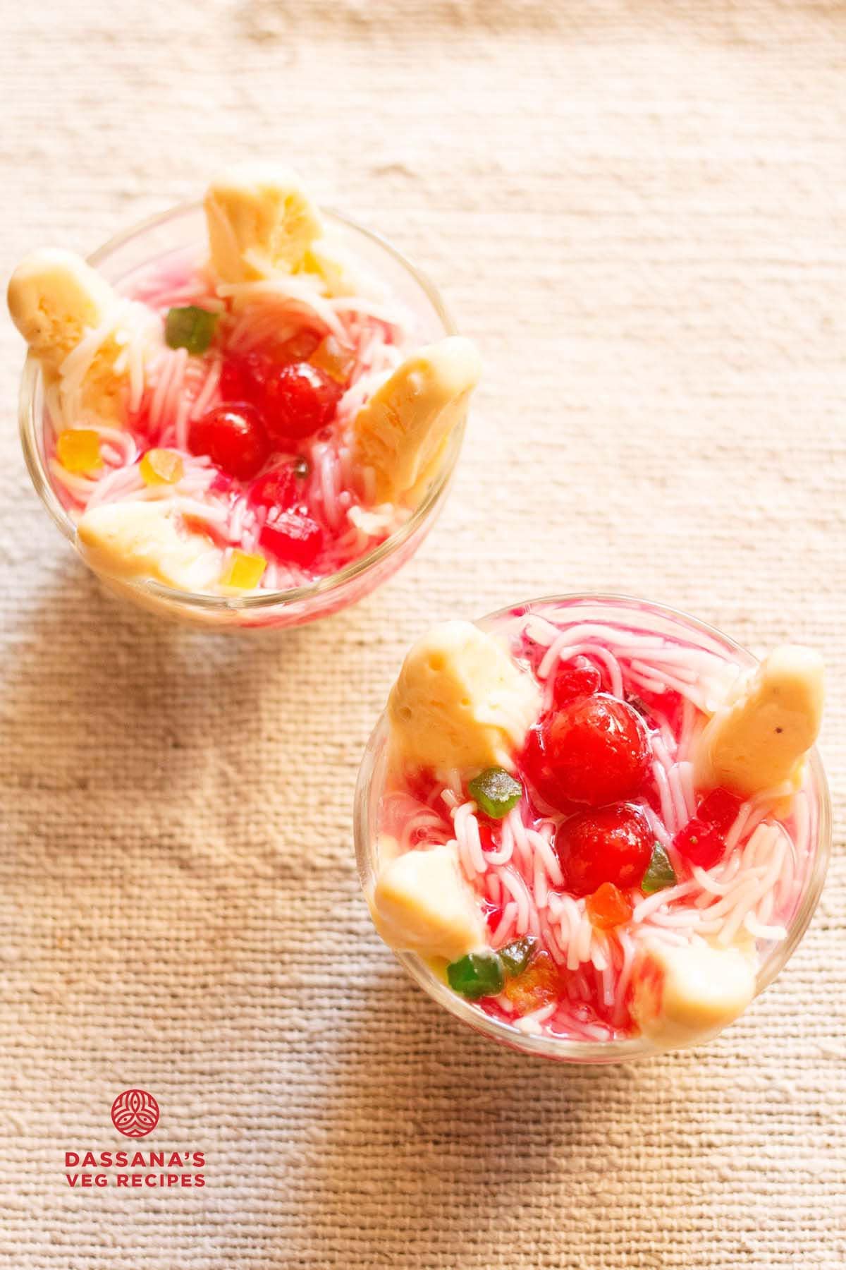 mango kulfi falooda topped with rose syrup, red cherries, tutti frutti in 2 bowls on a cream jute cloth.