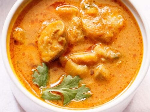 mushroom masala curry garnished with a coriander sprig in a white bowl.