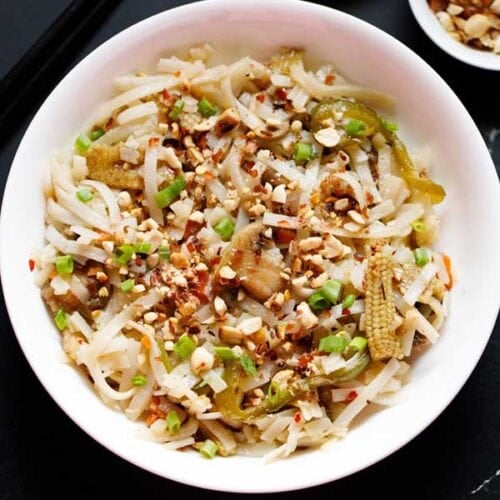 pad thai noodles in a white bowl garnished with crushed peanuts and spring onions.