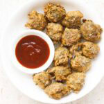 palak pakoda served in a white plate bowl with a side small bowl of ketchup on right side.
