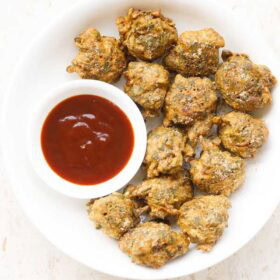 palak pakoda served in a white plate bowl with a side small bowl of ketchup on right side.