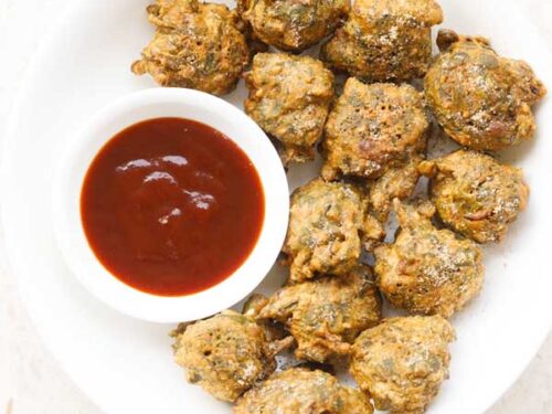 palak pakoda served in a white plate bowl with a side small bowl of ketchup on right side.