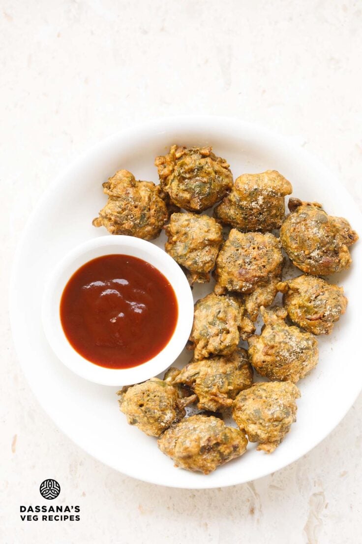 palak pakoda served in a white plate with a side bowl of ketchup on left side.