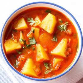 potato curry garnished with coriander leaves and served in a blue rimmed white bowl.