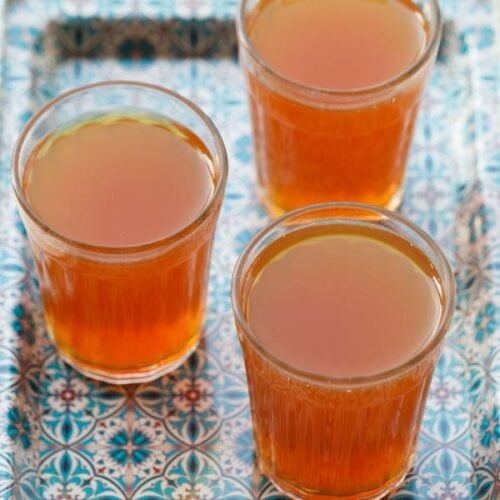 three glasses filled with sulaimani tea on a blue decorative tray.