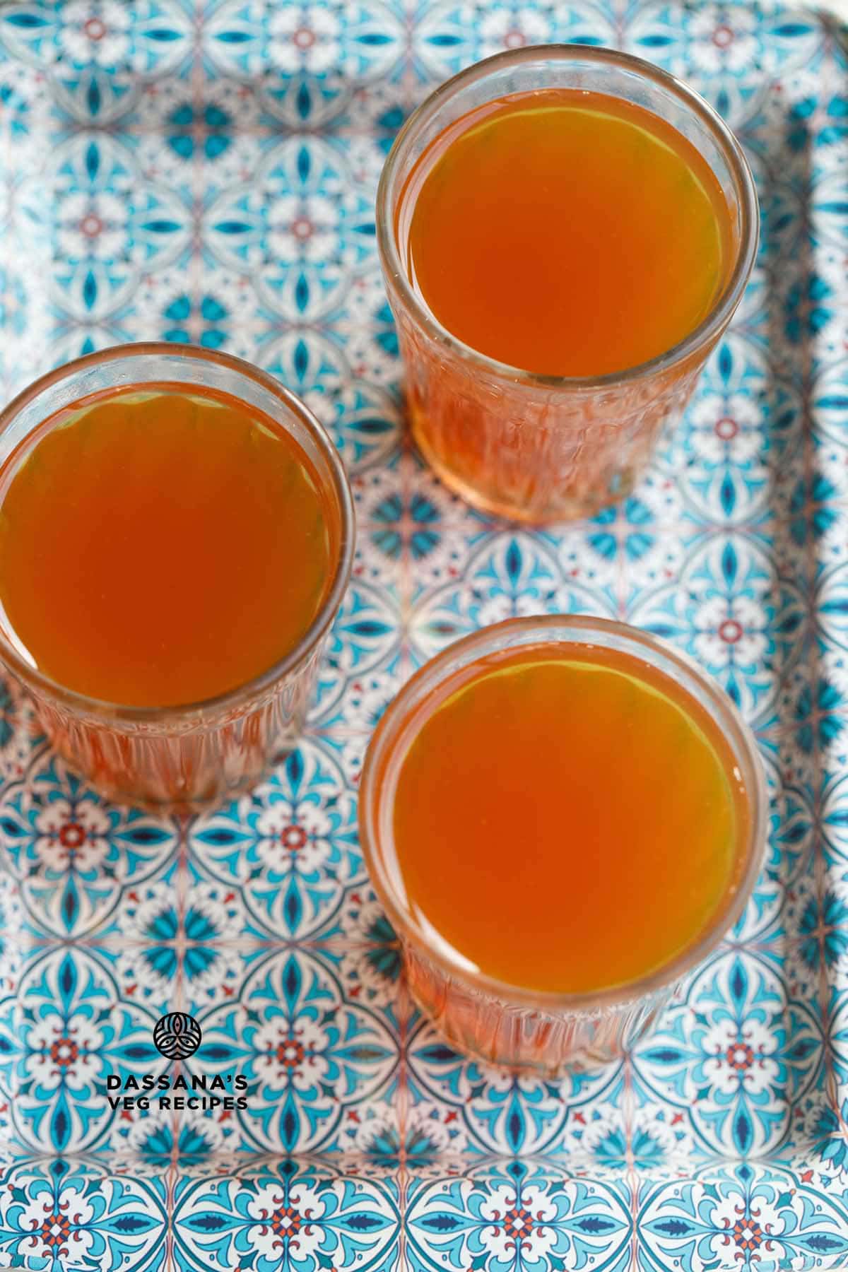 overhead shot of three glasses filled with sulaimani tea on a blue decorative tray.