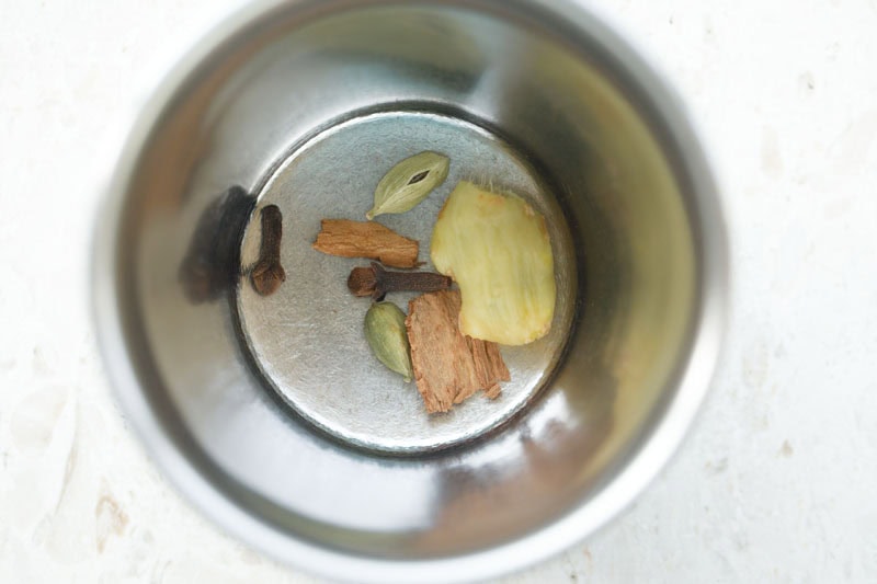 ginger and whole spices added to mortar. 